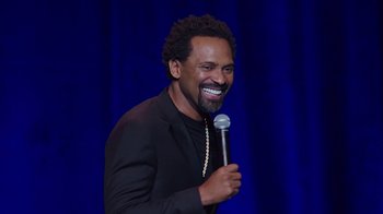 Movie still from “Mike Epps: Only One Mike” (2019), directed by Kevin Bray – A man holding a microphone while standing on a stage; Close Up shot, Over the shoulder angle