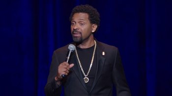 Movie still from “Mike Epps: Only One Mike” (2019), directed by Kevin Bray – A man in a black jacket holding a microphone; Close Up shot, High angle