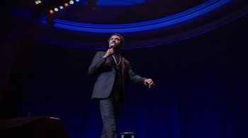 Movie still from “Mike Epps: Only One Mike” (2019), directed by Kevin Bray – A man in a black suit is holding a microphone; Medium shot, Low angle