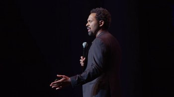 Movie still from “Mike Epps: Only One Mike” (2019), directed by Kevin Bray – A man holding a microphone while standing on a stage; Medium shot, High angle
