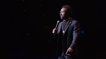 Movie still from “Mike Epps: Only One Mike” (2019), directed by Kevin Bray – A man holding a microphone while standing on a stage; Close Up shot, Over the shoulder angle