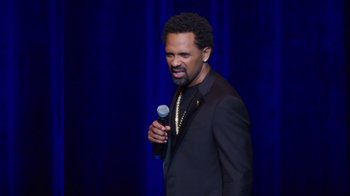 Movie still from “Mike Epps: Only One Mike” (2019), directed by Kevin Bray – A man holding a microphone while standing on a stage; Close Up shot, Over the shoulder angle