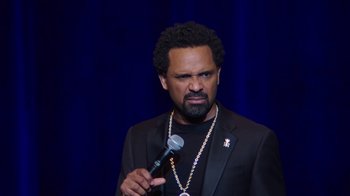 Movie still from “Mike Epps: Only One Mike” (2019), directed by Kevin Bray – A man in a black jacket holding a microphone; Close Up shot, Over the shoulder angle