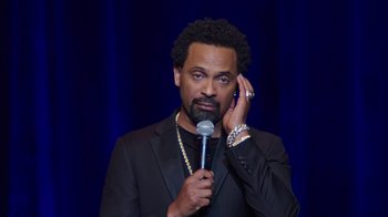 Movie still from “Mike Epps: Only One Mike” (2019), directed by Kevin Bray – A man holding a microphone in front of a microphone stand; Close Up shot, High angle