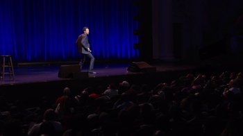 Movie still from “Mike Epps: Only One Mike” (2019), directed by Kevin Bray – A man sitting on a stage in front of an audience; Extreme Wide shot, High angle