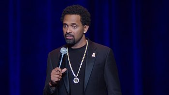 Movie still from “Mike Epps: Only One Mike” (2019), directed by Kevin Bray – A man in a black jacket holding a microphone; Close Up shot, Over the shoulder angle