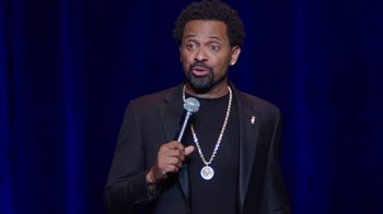 Movie still from “Mike Epps: Only One Mike” (2019), directed by Kevin Bray – A man in a black jacket holding a microphone; Close Up shot, Over the shoulder angle