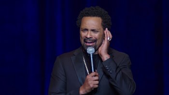 Movie still from “Mike Epps: Only One Mike” (2019), directed by Kevin Bray – A man holding a microphone up to his ear; Close Up shot, Over the shoulder angle