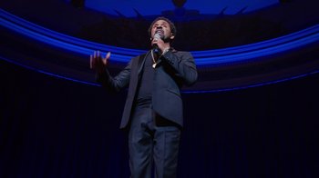 Movie still from “Mike Epps: Only One Mike” (2019), directed by Kevin Bray – A man in a black suit singing into a microphone; Medium shot, Low angle
