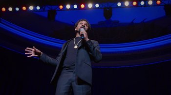 Movie still from “Mike Epps: Only One Mike” (2019), directed by Kevin Bray – A man in a black suit is holding a microphone; Medium shot, Low angle