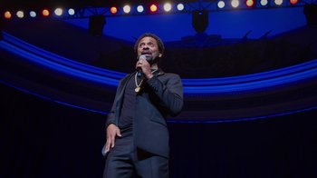 Movie still from “Mike Epps: Only One Mike” (2019), directed by Kevin Bray – A man in a black suit is holding a microphone; Medium shot, Low angle