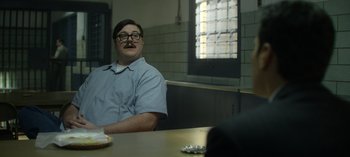 Movie still from “Mindhunter” (2017), directed by Tobias Lindholm – A man sitting at a table in front of a brick wall; Medium shot, Over the shoulder angle