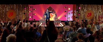 Movie still from “Little Miss Sunshine” (2006), directed by Jonathan Dayton – A man in a suit is on a stage with a microphone; Extreme Wide shot, Over the shoulder angle