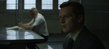 Movie still from “Mindhunter” (2017), directed by Tobias Lindholm – A man in a suit sitting at a table in front of another man in a suit; Close Up shot, Over the shoulder angle