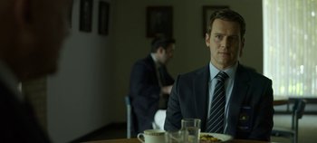 Movie still from “Mindhunter” (2017), directed by Tobias Lindholm – A man sitting at a table with food in front of him; Medium shot, Over the shoulder angle
