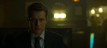 Movie still from “Mindhunter” (2017), directed by Tobias Lindholm – A man wearing a suit and tie sitting in front of a window; Close Up shot, Over the shoulder angle