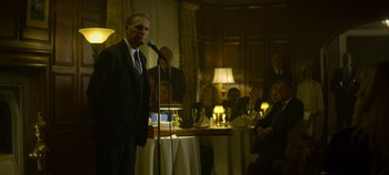 Movie still from “Mindhunter” (2017), directed by Tobias Lindholm – A man standing at a microphone in front of a group of people; Medium shot, Over the shoulder angle