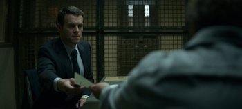 Movie still from “Mindhunter” (2017), directed by Tobias Lindholm – A man sitting at a table in a jail cell; Medium shot, Over the shoulder angle