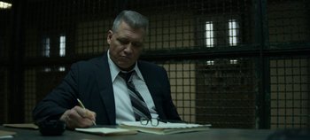 Movie still from “Mindhunter” (2017), directed by Tobias Lindholm – A man sitting at a table in front of papers; Close Up shot, Low angle