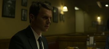 Movie still from “Mindhunter” (2017), directed by Tobias Lindholm – A man wearing a suit and tie in front of a table; Close Up shot, Over the shoulder angle