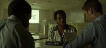 Movie still from “Mindhunter” (2017), directed by Tobias Lindholm – A man sitting at a table holding a paper; Close Up shot, Over the shoulder angle