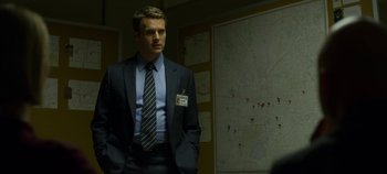 Movie still from “Mindhunter” (2017), directed by Tobias Lindholm – A man in a suit and tie standing in front of a map; Medium shot, Over the shoulder angle