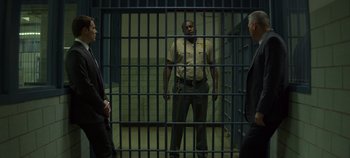 Movie still from “Mindhunter” (2017), directed by Tobias Lindholm – A man in a jail cell with two other men behind bars; Wide shot, Over the shoulder angle