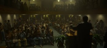 Movie still from “Mindhunter” (2017), directed by Tobias Lindholm – A crowd of people sitting and standing in front of a podium; Wide shot, High angle