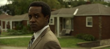 Movie still from “Mindhunter” (2017), directed by Tobias Lindholm – A man wearing a suit and tie standing in front of a house; Close Up shot, Over the shoulder angle