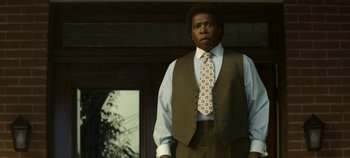 Movie still from “Mindhunter” (2017), directed by Tobias Lindholm – A man standing in front of a building wearing a suit and tie; Medium shot, Low angle