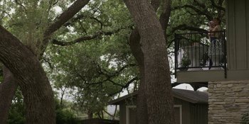 Movie still from “Love & Death” (2023), directed by Clark Johnson – A large tree with a house in the background; Extreme Wide shot, Low angle