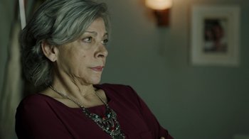 Movie still from “Money Heist” (2017), created by Álex Pina – An older woman wearing a red shirt and a necklace; Close Up shot, Low angle
