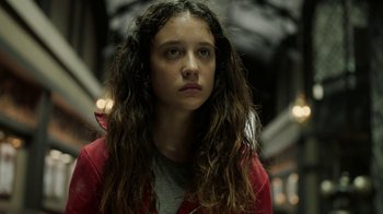 Movie still from “Money Heist” (2017), created by Álex Pina – A young woman with long , curly hair stares into the camera; Close Up shot, Low angle