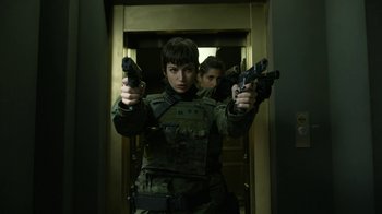 Movie still from “Money Heist” (2017), created by Álex Pina – A woman holding two pistols while standing next to a door; Medium shot, Low angle