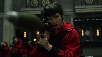 Movie still from “Money Heist” (2017), created by Álex Pina – A woman holding a gun while standing in a room; Medium shot, Low angle