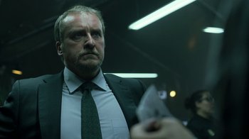 Movie still from “Money Heist” (2017), created by Álex Pina – A man in a suit and tie looking at someone; Close Up shot, Low angle