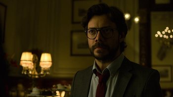 Movie still from “Money Heist” (2017), created by Álex Pina – A man in a suit and tie standing in front of a lamp; Close Up shot, Low angle