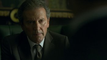 Movie still from “Money Heist” (2017), created by Álex Pina – An older man wearing a suit and tie; Close Up shot, Over the shoulder angle