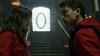 Movie still from “Money Heist” (2017), created by Álex Pina – A man and a woman standing next to each other in front of a staircase; Close Up shot, Over the shoulder angle