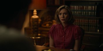 Movie still from “Love & Death” (2023), directed by Clark Johnson – A woman sitting at a table in front of a lamp; Medium shot, Over the shoulder angle