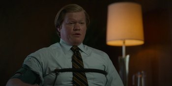 Movie still from “Love & Death” (2023), directed by Clark Johnson – A man in a suit and tie with a tie around his neck; Medium shot, High angle