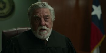 Movie still from “Love & Death” (2023), directed by Clark Johnson – An older man in a black gown and white beard; Close Up shot, High angle