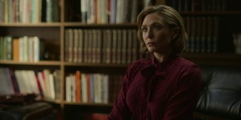Movie still from “Love & Death” (2023), directed by Clark Johnson – A woman wearing a red shirt in front of a book shelf; Medium shot, Over the shoulder angle