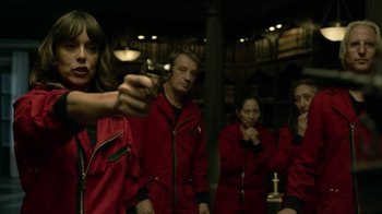 Movie still from “Money Heist” (2017), created by Álex Pina – A woman holding a gun in front of a group of people; Medium shot, Over the shoulder angle