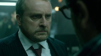 Movie still from “Money Heist” (2017), created by Álex Pina – A person wearing a suit and tie; Close Up shot, Over the shoulder angle