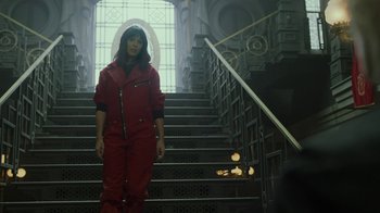Movie still from “Money Heist” (2017), created by Álex Pina – A woman in a red jumpsuit standing on a set of stairs; Wide shot, Low angle