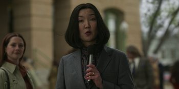 Movie still from “Love & Death” (2023), directed by Clark Johnson – A woman holding a microphone in her hands; Close Up shot, Low angle