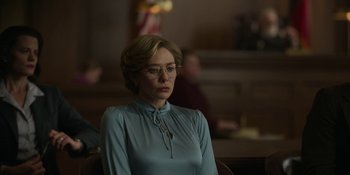 Movie still from “Love & Death” (2023), directed by Clark Johnson – A woman in a blue dress sitting in front of a group of people; Medium shot, Low angle