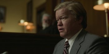 Movie still from “Love & Death” (2023), directed by Clark Johnson – A man wearing a suit and tie in a courtroom; Close Up shot, Low angle