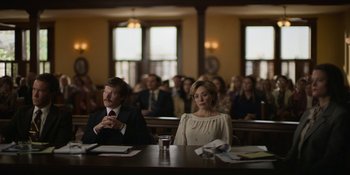 Movie still from “Love & Death” (2023), directed by Clark Johnson – A man and a woman sitting at a table in front of an audience; Medium shot, Low angle